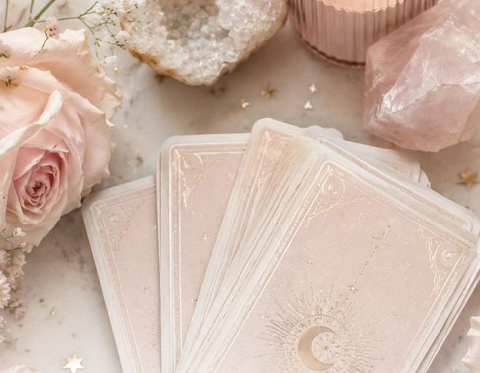 Baraja de tarot extendida entre rosas y cuarzos rosados