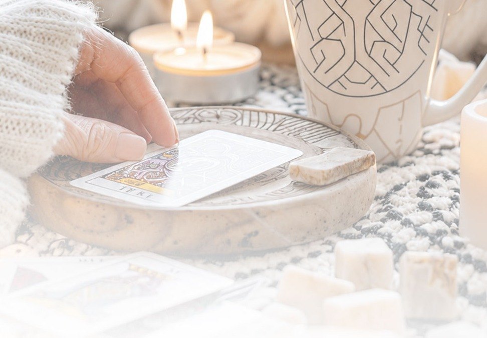 Manos tomando una carta junto a una taza humeante y velas